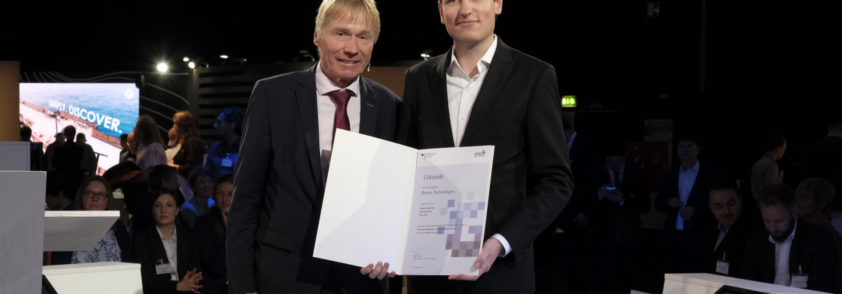 Ministerialdirigent Andreas Goerdeler überreicht Breeze Technologies-Mitgründer Robert Heinecke die Urkunde zum Gründerpreis - Digitale Innovationen